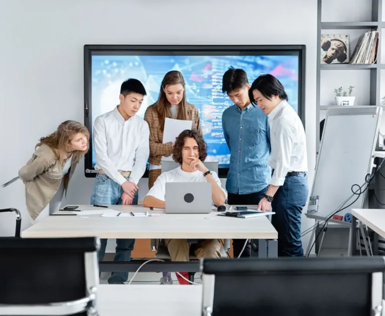 A team gathered around a laptop and a large screen during a working session