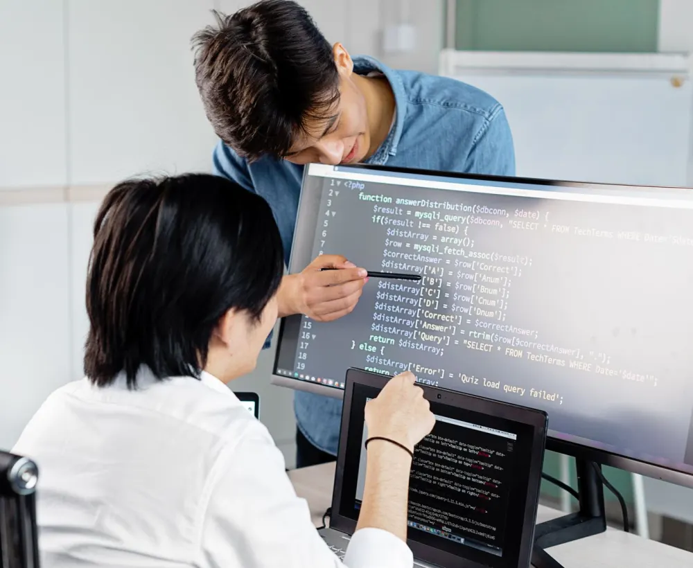 Two developers reviewing code together on a large monitor